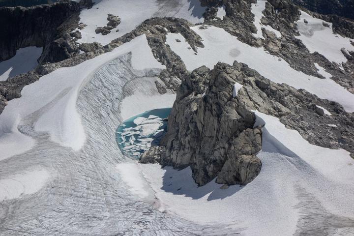 Snow-covered alpine bowl with a turquoise meltwater pool beside a rock outcrop