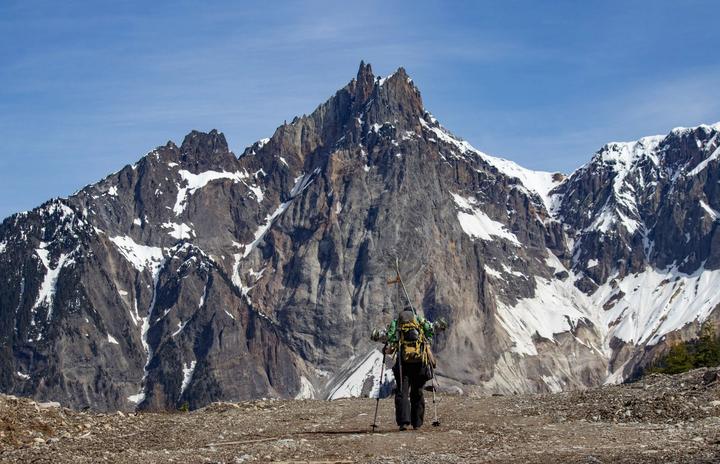 Hiker with trekking poles beneath a jagged rocky peak