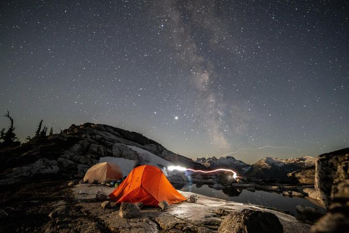 Orange tent glowing under the Milky Way on a mountain ridge