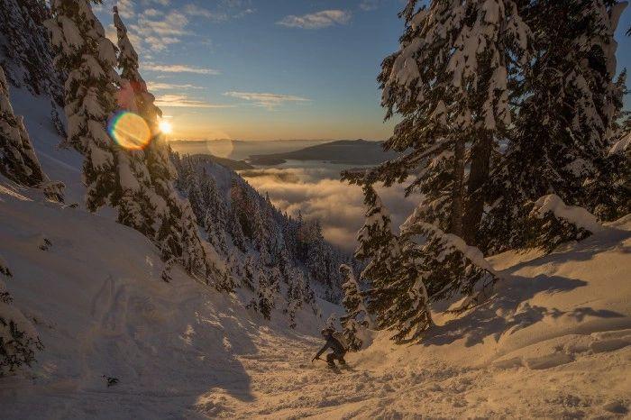Skier in a snowy gully at sunset above a sea of clouds