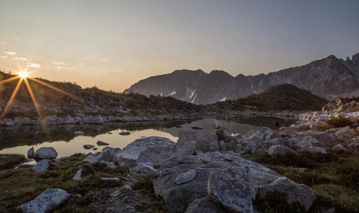 Sunburst over an alpine tarn and boulders