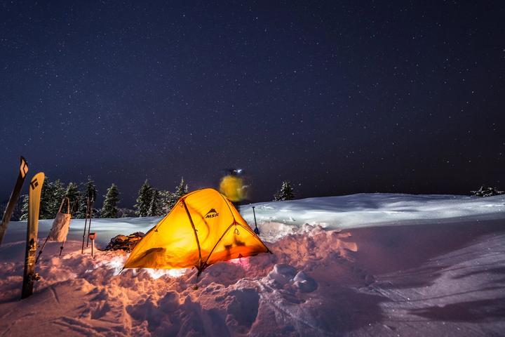 Tent lit from within on a snowy ridge at night